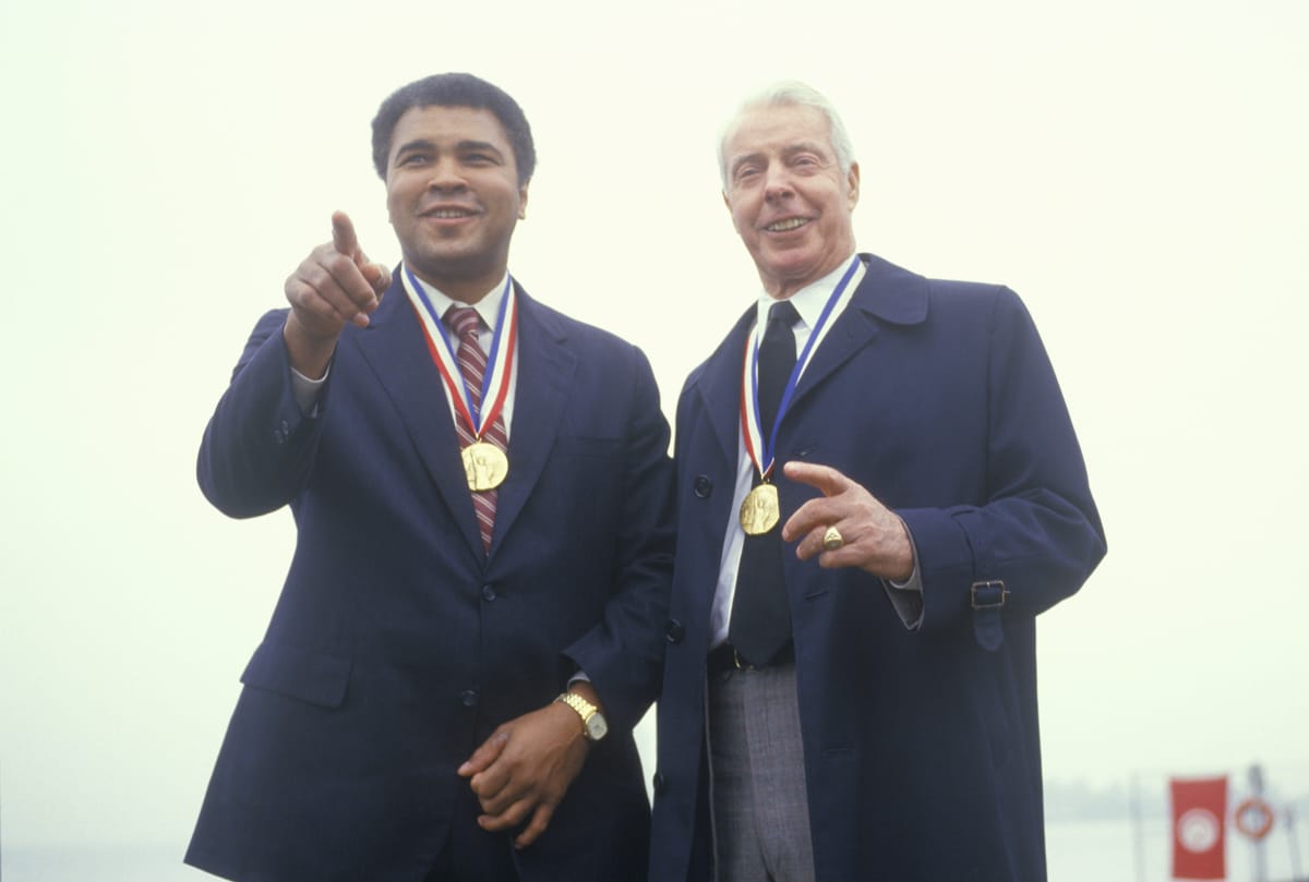Muhammed Ali and Joe DiMaggio wearing gold medals, Ellis Island, NY